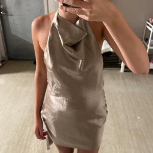 Beige satin klänning - Beige fin satin klänning med öppen rygg och knytning vid nacken. Helt ny med prislapp kvar!