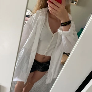 Vit oversized skjorta i bomull - Säljer en klassisk vit skjorta i bomull med lång ärm och knappar framtill. Skjortan har en avslappnad, oversized passform och bröstficka. Perfekt att styla öppen över ett linne eller knäppt för en clean look.