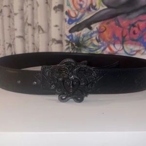 Svart versace bälte  - Snyggt svart versace bälte i skinn med präglat mönster och ett riktigt coolt spänne format som en orm. Bältet har en stilren look med detaljer som sticker ut och passar perfekt för att lyfta vilken outfit som helst. Pris går givetvis att diskutera.
