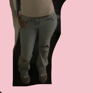 Nelly Ljusblå bootcut jeans med slitningar och rosa fickor  - Säljer ett par ljusblå jeans med bootcut passform och snygga slitningar vid knäna. Jeansen har klassisk femficksdesign och låg midja. Perfekta för en avslappnad och trendig look. Lite slitna där nere. Köpte för 699 säljer för 650 men pris kan diskuteras 
