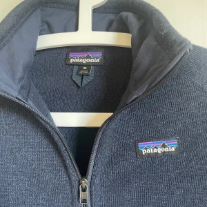 Patagonia fleece - En riktigt härlig fleece från Patagonia. | Den är i mycket bra skick och har inga skador eller liknande som bör anmärkas. | Den har mycket fin mörkblå färg som matchar med loggan. | Den har mycket bra förvarings möjligheter eftersom den har två vanliga fickor framtill med dragkedja, en ficka med dragkedja på vänster arm och två inner fickor utan dragkedja. | Det är bara at kontakt mig om man vill ha bild på inner fickorna eller annat. Och har även några extra bilder om man vill ha det. Mvh Leo🤗