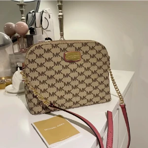 Michael Kors axelväska beige färg med brun logga ⭐️  - Unik axelväska från Michael Kors i beige färg med bruna MK-loggor över hela väskan. Unik färg som är svår att hitta någon annanstans. Guldiga detaljer, kedjerem och justerbar axelrem i rosa. Väskan har dragkedja upptill och flera fack inuti. Perfekt storlek för det viktigaste. Självklart äkta ⭐️ 