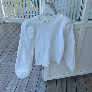 Vit puffärmströja från Gina Tricot - Säljer en vit långärmad tröja från Gina Tricot med trendiga puffärmar och rund halsringning. Tröjan är i mjuk bomull och har en clean, stilren look som passar perfekt till jeans eller kjol. Enkel att styla för en fräsch vardagsoutfit.