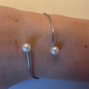 Silvrigt armband med pärldetaljer+ring - Stilrent armband i silverfärgad metall med två vita pärlor i ändarna. Öppen design som gör det lätt att ta på och av. Perfekt för dig som gillar minimalistiska smycken med en touch av elegans. En silvrig ring. Handgjort 