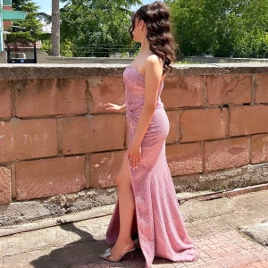 Glittrig rosa festklänning med slits - Säljer en superfin glittrig rosa långklänning med axelbandslös design och hög slits. Klänningen har figurnära passform och markerad midja, perfekt för bal eller fest. Materialet är glittrigt och skimrar snyggt i ljuset.