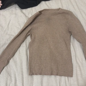 Beige ribbad långärmad tröja - En beige, ribbad långärmad tröja med rund halsringning. Tröjan är figurnära och har en enkel, stilren design som passar perfekt till jeans eller kjol. Materialet känns mjukt och stretchigt, vilket gör den bekväm att bära hela dagen.