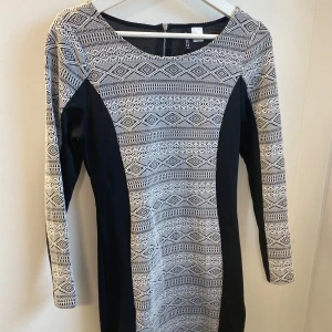 Svartvit mönstrad klänning H&M - Snygg svartvit klänning från H&M med grafiskt mönster och lång ärm. Klänningen har figurnära passform, dragkedja bak och är tillverkad i ett stretchigt material som sitter bekvämt. Perfekt för dig som gillar stilrena kontraster och coola detaljer.