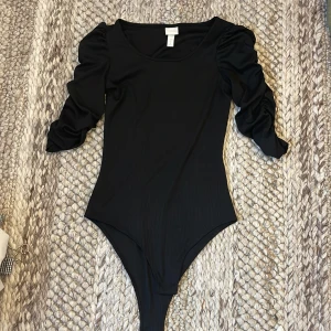 Svart ribbad topp med puffärm H&M XS - Svart ribbad topp från H&M i storlek XS med snygga puffärmar och rund halsringning. Toppen har en figurnära passform och är tillverkad i ett stretchigt material. 