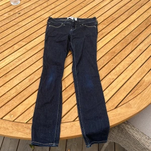 Mörkblå slim jeans från Abercrombie - Snygga mörkblå slim jeans från Abercrombie Kids i modellen jean legging. Byxorna har klassiska fickor med dekorativ brodyr bak, kontrastsömmar och smal passform. 