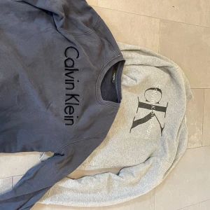 Calvin Klein sweatshirts i grått & svart - Två Calvin Klein sweatshirts båda i storlek large. Finns att hämta i Bromma. Går att köpa styckvis för 175kr