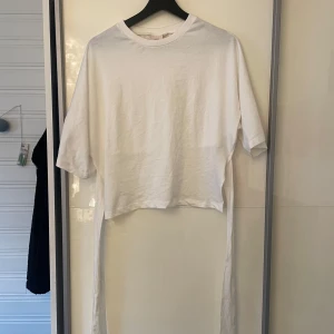 Vit t-shirt med knyt från Nelly - Snygg vit t-shirt från Nelly med korta ärmar och långa knytband i sidorna. Tröjan är aldrig använd utan endast provad.
