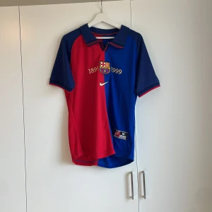 Barcelona jubileumströja Nike M - Säljer en officiell FC Barcelona jubileumströja från Nike i storlek M. Tröjan har klassisk halva röd och halva blå design med klubbmärke och årtalen 1899-1999 broderat på bröstet. Tillverkad i lätt och ventilerande Dri-FIT-material, perfekt för fotboll eller supporterliv.