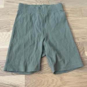 Ribbade gröna shorts från H&M Divided - Snygga ribbade shorts i en dämpad grön färg från H&M Divided. Modellen är midwaist och har en bekväm, elastisk midja. Materialet är mjukt och stretchigt, perfekt för chill dagar eller när du vill ha en avslappnad look.