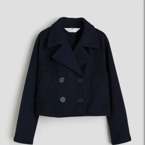 Mörkblå kappa från H&M - Säljer en stilren mörkblå kappa/ höstjacka från H&M med dubbelknäppning och bred krage. Jackan är croppad och har två snedställda fickor framtill. Perfekt för dig som vill ha en klassisk look med modern twist.