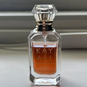 Kayali Utopia Vanilla Coco 21 Parfym - Kayali Utopia Vanilla Coco 21 är en lyxig parfym i en elegant, genomskinlig glasflaska med guldiga detaljer och en kristalliknande kork. Doften har inslag av vanilj och kokos, perfekt för dig som gillar söta och exotiska toner.