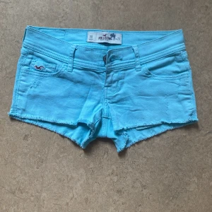 Turkosa jeansshorts från Hollister - Supersnygga turkosa jeansshorts från Hollister med råa kanter och klassisk femficksdesign. Shortsen har låg midja och är tillverkade i mjuk bomull med lite stretch. Perfekta för varma sommardagar. Storlek 23 men passar nog även 24. Säljer då jag råkade beställa i fel storlek så dom är alldrig använda. Väldigt lågmidjade.