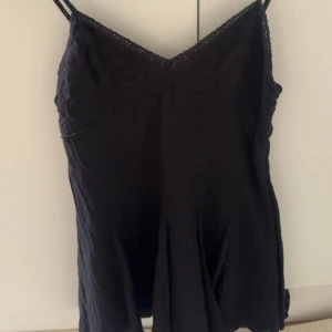 Svart klänning från Zara - Supersnygg svart klänning från Zara med tunna axelband och v-ringad spets upptill. Klänningen har en flowy passform. Materialet känns lätt och luftigt, och spetsdetaljerna ger en extra touch.