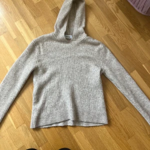 Beige ribbad hoodie från Weekday - Mysig beige hoodie från Weekday i ribbstickad design. Tröjan har lång ärm, huva och är gjord i ett mjukt stickat material som passar perfekt när det är kallt. Enkel och stilren modell som är lätt att matcha med allt.