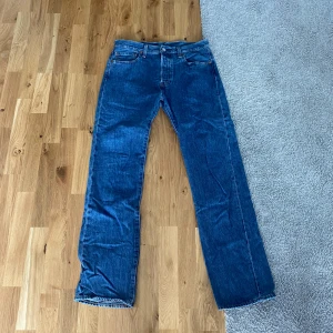Blå Levi’s 501 Jeans 501 33/34 - Klassiska Levi's 501 jeans i blå denim med raka ben och normal passform. Byxorna har fem fickor, knappgylf och den ikoniska läderpatchen bak i midjan. Perfekta för dig som gillar tidlös stil och vill ha ett par schyssta jeans i bomull. Skick 8/10.