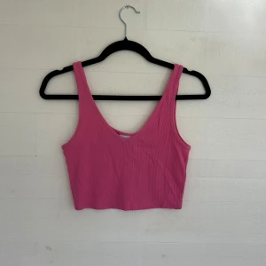 Rosa ribbad linnetopp från Weekday - Säljer en rosa croppad linnetopp från Weekday i ribbad bomull. Toppen har breda axelband, v-ringning och ärmlös design. Perfekt för varma dagar eller att styla lager på lager. Superenkel att matcha med jeans eller kjol.