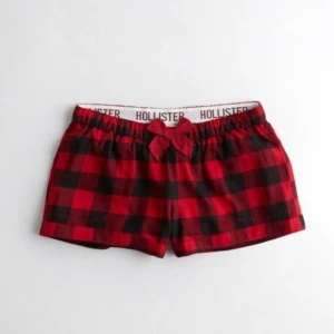 Rödrutiga shorts från Hollister - Superfina rödrutiga shorts från Hollister med elastisk midja och en söt rosett framtill. Klassisk rutig design i rött och svart, perfekta för chill dagar hemma. Mjukt bomullsmaterial som känns skönt mot huden.