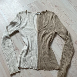 Ribbad v-ringad tröja från NA-KD - Superfin ribbad tröja från NA-KD i tvåfärgad design, beige och vit. V-ringad med lång ärm och figurnära passform. Snyggt mönster med breda vertikala ränder och lätt vågig nederkant. Perfekt för dig som gillar stilrena och trendiga plagg.