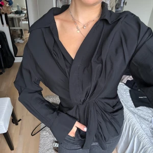 Svart omlottblus med knyt - Snygg svart omlottblus med knyt i midjan och v-ringad hals. Köpt från About You