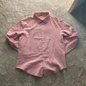 Rosa skjorta  - Snygg rosa skjorta med klassisk krage och knäppning framtill. Skjortan har lång ärm och en rak passform, perfekt för en stilren look. Tillverkad i mjukt bomullstyg som känns skönt mot huden.