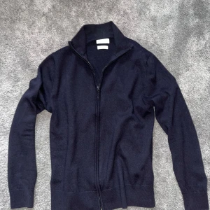 Fullzip från these glory days - Säljer en marinblå stickad kofta med dragkedja och hög krage. Perfekt för lager-på-lager och enkel att matcha med olika outfits. Klassisk och stilren design.
