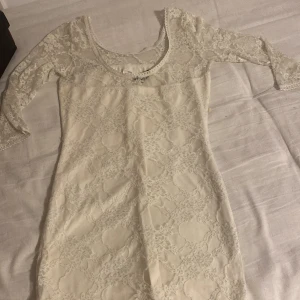 Vit spetsklänning från Divided - Säljer en söt vit spetsklänning från Divided med trekvartsärm och rund halsringning. Klänningen har ett genomgående blommigt spetsmönster och är figurnära i modellen. Perfekt för vår och sommar!