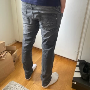 Grå Replay Anbass jeans slim fit - Säljer ett par gråa Replay Anbass jeans i slim fit med klassisk femficksdesign och snygga detaljer på bakfickorna. Byxorna har midwaist och är i stretchigt material för skön passform. Midjemått W34 och längd L32.