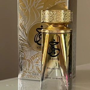 Khair Felicity Eau de Parfum från Paris Corner - Lyxig parfym i en guldig, geometrisk flaska med detaljerad kork. Flaskan rymmer 100 ml och har en exklusiv design med arabiska och engelska inskriptioner. Kommer i en elegant förpackning med guld- och silvermönster. Ca 10 sprut tagna från flaskan. Nypris 399