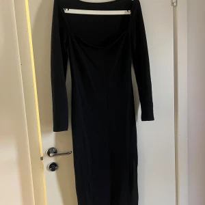 Svart långärmad klänning i bomull - En stilren stickad svart långklänning med lång ärm och u- ringad halsringning. Klänningen har en tight passform i mjukt material, vilket gör den både bekväm och enkel att styla. Perfekt för dig som gillar minimalistisk och tidlös design.