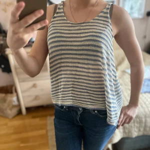 Randig linnetopp i blått och vitt - Säljer en luftig och somrig linnetopp med blå och vita ränder. Toppen är ärmlös och har en avslappnad passform, perfekt för varma dagar. Snygg att matcha med jeans eller shorts!