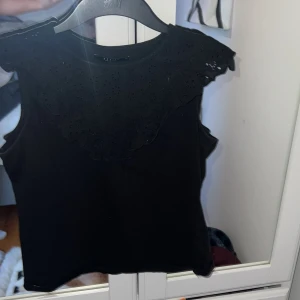 Svart ärmlös topp med spetsdetaljer - Säljer en svart ärmlös topp från Mohito med vacker spets runt axlar och halsringning. 