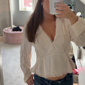 Blus med v-ringning och volang - Säljer en söt ”beige” blus med v-ringning och långa ärmar. Blusen har volangdetaljer vid nederkanten och är perfekt att styla med jeans eller kjol för en fräsch look🫰🏼🫰🏼Kan säkert strykas!!