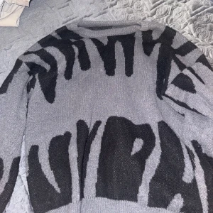 Grå och svart stickad tröja med zebramönster - Säljer en stickad tröja i grått och svart med coolt zebramönster. Tröjan har lång ärm och en avslappnad passform. Ny tröja.