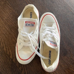 Vita Converse All Star sneakers - Klassiska vita Converse All Star sneakers med röd rand runt sulan och vita snören. Låg modell med rund tå och platt sula. Perfekta för en avslappnad och stilren look.