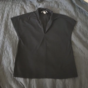 Svart topp med krage från H&M - Säljer en svart topp från H&M i storlek XS. Toppen har en lös passform med korta ärmar och en snygg krage som ger en stilren look. Perfekt att matcha med jeans eller kjol för en enkel och trendig outfit.❣️