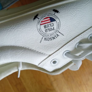 Vita sneakers från Vinson Polo Club - Säljer ett par fräscha vita sneakers från Vinson Polo Club med klassisk design och logga på sidan. Skorna har snörning och är tillverkade i syntetmaterial med rund tå och platt sula. Perfekta för en stilren och sportig look.