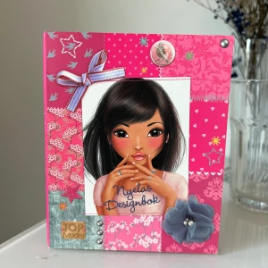 Top Model Designbok - En kreativ designbok från Top Model med färgglad framsida, illustrationer och plats för egna skisser. Innehåller sidor för att designa kläder och skor, perfekt för dig som gillar mode och att rita egna kreationer. Två sidor är ritade i men annars i bra skick