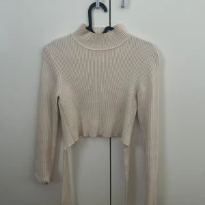 Beige croppad topp med öppen rygg  - Säljer en beige croppad polotopp i ribbat material med öppen rygg. Tröjan har långa ärmar öppen rygg med knyte som kan knytas bak eller fram. Från Zara i storlek S