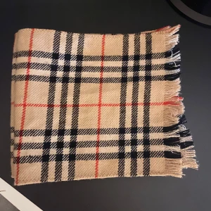 Beige rutig burberry halsduk - Snygg beige burberry halsduk med klassiskt rutigt mönster i svart, vitt och rött. Halsduken har fransar i kanterna och känns både stilren och tidlös. Perfekt accessoar för att lyfta din outfit under kyliga dagar. 800kr, på för byten osså