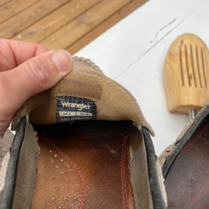 Beige mockaloafers från Wrangler - Säljer ett par beige loafers från Wrangler i mocka med kontrastdetaljer i mörkgrått. Skorna har rund tå, platt sula och dekorativa sömmar runt ovandelen. Perfekta för en avslappnad och stilren look.