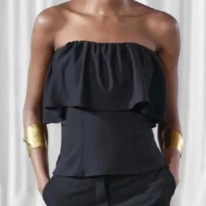 Svart axelbandslös volangtopp - Säljer en svart axelbandslös topp med volangdetalj upptill. Ifrån Zara, ny med prislapp kvar, storlek S.