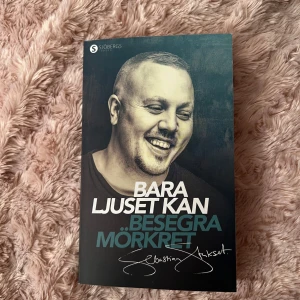 Bara ljuset kan besegra mörkret - En bok med titeln 'Bara ljuset kan besegra mörkret' från förlaget Sjöbergs. Omslaget har en porträttbild i svartvitt av en leende man och text i vitt och blått. Perfekt för dig som gillar inspirerande och personliga berättelser.