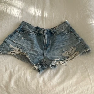 Ljusblå jeansshorts med fransar - Säljer ett par ljusblå jeansshorts med slitna detaljer och fransar längs kanterna. Klassisk femficksmodell med dragkedja och knapp framtill. Perfekta för varma dagar nu i sommar skriv vid frågor!