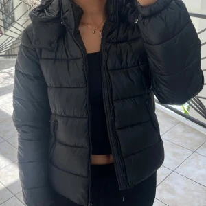 Svart pufferjacka med huva - Säljer en svart pufferjacka med huva och dragkedja framtill. Jackan har långa ärmar och två fickor med dragkedja på sidorna. Perfekt för kyligare dagar och enkel att matcha med olika outfits. Pris går att diskutera.