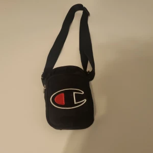 Champion wristbag (Svart) - Har plats till mycket t ex Nycklar, Mobil och Laddare. Har tre fack och du kan justera hur den ska sitta på dig