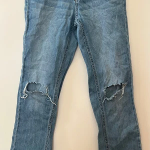 Blå jeans med slitningar från LAB Industries - Säljer ett par blå jeans från LAB Industries med slitna hål på båda knäna. Klassisk femficksmodell med knapp och dragkedja i gylfen. Jeansen har en rak passform och är tillverkade i denim. Är inte använda för att det blev fel storlek.